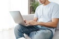 Young man sitting on the sofa at home typing on the laptop keyboard for online working, using internet, freelancer, relaxed,