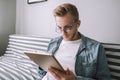 Young man sitting on a sofa uses a tablet computer with white screen. mock up Royalty Free Stock Photo