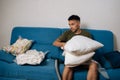 Young man sitting on sofa, using vacuum storage bag to organize and compress bedding, efficiently creating space-saving Royalty Free Stock Photo