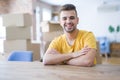 Young man sitting on the table with cardboard boxes behind him moving to new home happy face smiling with crossed arms looking at Royalty Free Stock Photo