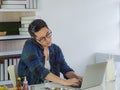 A young man is sitting and talking on a mobile phone and using a laptop on the table in the office. Royalty Free Stock Photo