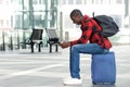 Young man sitting on traveling bag and using cell phone
