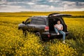 Young man sitting in the trunk of a car in yellow rape field Royalty Free Stock Photo