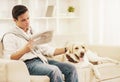 Young Man Sitting on White Sofa with Dog at Home. Royalty Free Stock Photo