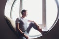 young man sitting in a window looking out over the city . Men enjoy sun in window of hotel room. Royalty Free Stock Photo