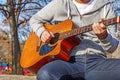 Young man sitting on wooden chair in park and playing guitar Royalty Free Stock Photo