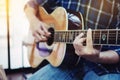 A young man sitting on wooden chair and plays acoustic guitar