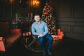 Young man sitting on the wooden horse near Christmas tree with presents and lights in dark living room Royalty Free Stock Photo