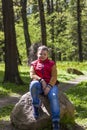 A young man in a sleeveless red jacket is sitting on a huge stone in a pine forest in spring. The magical light from the sun`s Royalty Free Stock Photo