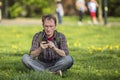 Young man with smartphone sitting on the grass in a city Park.