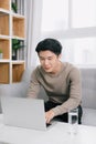 Young man smiling as he reads the screen of a laptop computer while relaxing on a comfortable couch at home Royalty Free Stock Photo