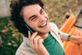 Young man smiling broadly and talking on mobile phone with his friend against white cocnrete wall. Handsome male with curly hair Royalty Free Stock Photo