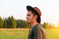 Young man smiling farmer in cowboy hat at agricultural field on sunset with sun flare. Profile portrait of millennial