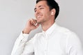 Young man smiling, having a call via wireless earphones with a colleague on white wall. Caucasian businessman wearing