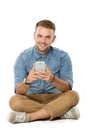 Young man smiling while holding his cellphone, sitting on the fl Royalty Free Stock Photo