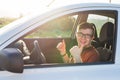 Young man smiling and showing thumbs up in his car. Auto purchase and people concept