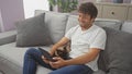 Young man smiling while using tablet and cuddling with cat on couch indoors Royalty Free Stock Photo
