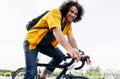 Young man smiling and wearing yellow shirt with backpack and his bike walking in the city street. Male courier with curly hair Royalty Free Stock Photo