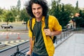 Young man smiling and wearing yellow shirt with backpack and his bike walking in the city street. Male courier with curly hair Royalty Free Stock Photo