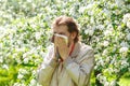 The young man sneezes on a background of a blossoming Apple tree