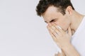 A young man sneezes into a napkin. Isolated white background