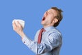 Young man sneezing with open mouth and handkerchief in office Royalty Free Stock Photo