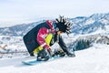 Young man snowboarder in fanny hat sits in the snow and fastens fastenings on a snowboard before the descent Royalty Free Stock Photo