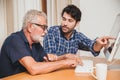 Young man or son teaching his grandfather elderly dad learning to using computer at home Royalty Free Stock Photo