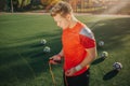 Young man in sport uniform is ready to exercise using jump rope. He looks down. Guy stand on green lawn. Five football Royalty Free Stock Photo