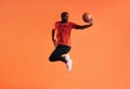 Young man in sportswear practicing basketball against an orange background. African male athlete jumping in the air with basket Royalty Free Stock Photo