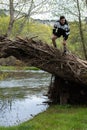 Young man in sportswear and shorts climbing on a fallen tree trunk laughing after having achieved the triumph with a stream below Royalty Free Stock Photo