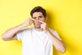 Young man squeezing pimple on nose, standing over yellow background. Concept of skin care and acne Royalty Free Stock Photo