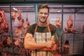 Young man stand at meat shelf in grocery store. He hold butcher knife in hand and pose. Animal brawn behind. Positive