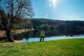 Young man stand on nice clean pond with wooden building and spring tree with blue sky