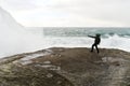 Young man standing on cliffs in front of the wild ocean with waves clashing against the rocks at Bunes Beach on Lofoten Islands in