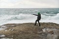 Young man standing on cliffs in front of the wild ocean with waves clashing against the rocks at Bunes Beach on Lofoten Islands in