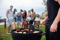 Young man standing and cooking sauseges on barbeque party