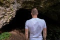 Young man standing in front of a cave entrance and looking into the darkness Royalty Free Stock Photo