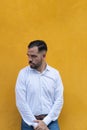 Young man standing in front of a yellow wall. He is looking to the side with seriousness