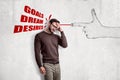 Young man standing half-turn, hand at forehead, at wall with drawing of big finger gun shooting words `Goals, Dream