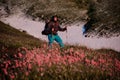 Young man standing on the hill field with hiking backpack and sticks in the foreground of pink flowers Royalty Free Stock Photo
