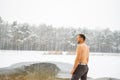 Young man standing by ice hole and ready to swim in the winter water