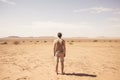 A young man standing in the middle of the desert and looking at the horizon, Male tourist standing in front of a sandy beach and Royalty Free Stock Photo
