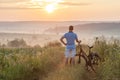 Young man standing near bicycle in morning sunrise with wonderf Royalty Free Stock Photo