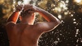 A young man is standing in a river and washing his face against the sunset.