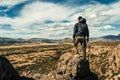 Young man standing on a rock at the top of a cliff overlooking a valley with a mountain range in the background. Royalty Free Stock Photo
