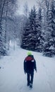 Young man standing among snowy trees in winter forest and enjoying first snow. Wearing hat and bagpack on travel