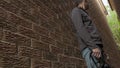 High quality picture of a young man who is standing between two red brick walls and holding photo camera in his hands