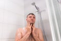 Young man standing under flowing water in shower cabin