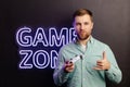 Young man standing at the wall in the room and playing, holding wireless joystick, screaming, and winning intense video game match